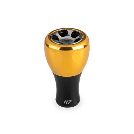 Der Taken H7 Knob 40mm von Taken ist ein goldener Aluminium-Stimmknopf für Baitcaster und Spinnrollen (Shimano und Daiwa). Er hat eine metallische Oberfläche mit vier kreisförmigen Aussparungen und einer "H7"-Markierung auf weißem Hintergrund.