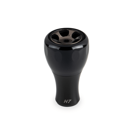 Ein schwarzer Taken H7 Knob 40mm - Aluminium Tuning Knauf, entworfen für Shimano & Daiwa Baitcaster und Spinnrollen, wird vor einem weißen Hintergrund gezeigt. Die metallisch glänzende Oberseite weist fünf kreisförmige Öffnungen und ein Branding im unteren Teil auf.