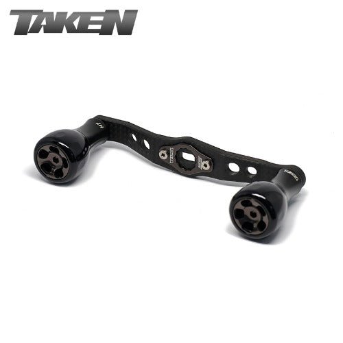 Ein Taken H7 SS Crossover Carbon Griff 100 mm in Schwarz, mit H7 Aluminium Knobs für Shimano & Daiwa, und TAKEN Logo oben links auf weißem Hintergrund.