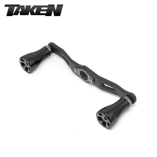 Der Taken One11 A2 Carbon Griff (111 mm) in Schwarz verfügt über zwei ergonomische A2 Aluminium Knöpfe und passt auf Shimano und Daiwa Rollen, die auf einem weißen Hintergrund mit dem TAKEN Logo abgebildet sind - ideal für das Werfen großer Swimbaits.