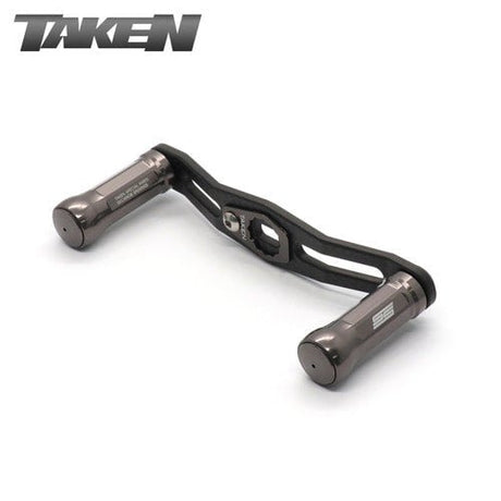Der Taken SS Carbon Griff 85 mm in gunmetal verfügt über SS Aluminiumknöpfe und ist ideal für Shimano & Daiwa Finesse-Baitcaster Setups; der TAKEN Markenname erscheint in der oberen linken Ecke.