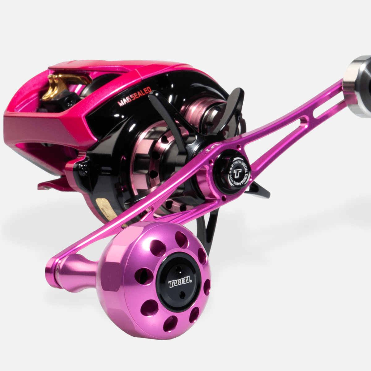 Eine Nahaufnahme des Taken X3 Knob 50mm - Power Tuning Knauf für Shimano & Daiwa Angelrollen von Taken, dargestellt in Pink und Schwarz mit metallischen Akzenten und Tuned XL Label - ideal für Hecht & Bigbait Angler - auf weißem Hintergrund.