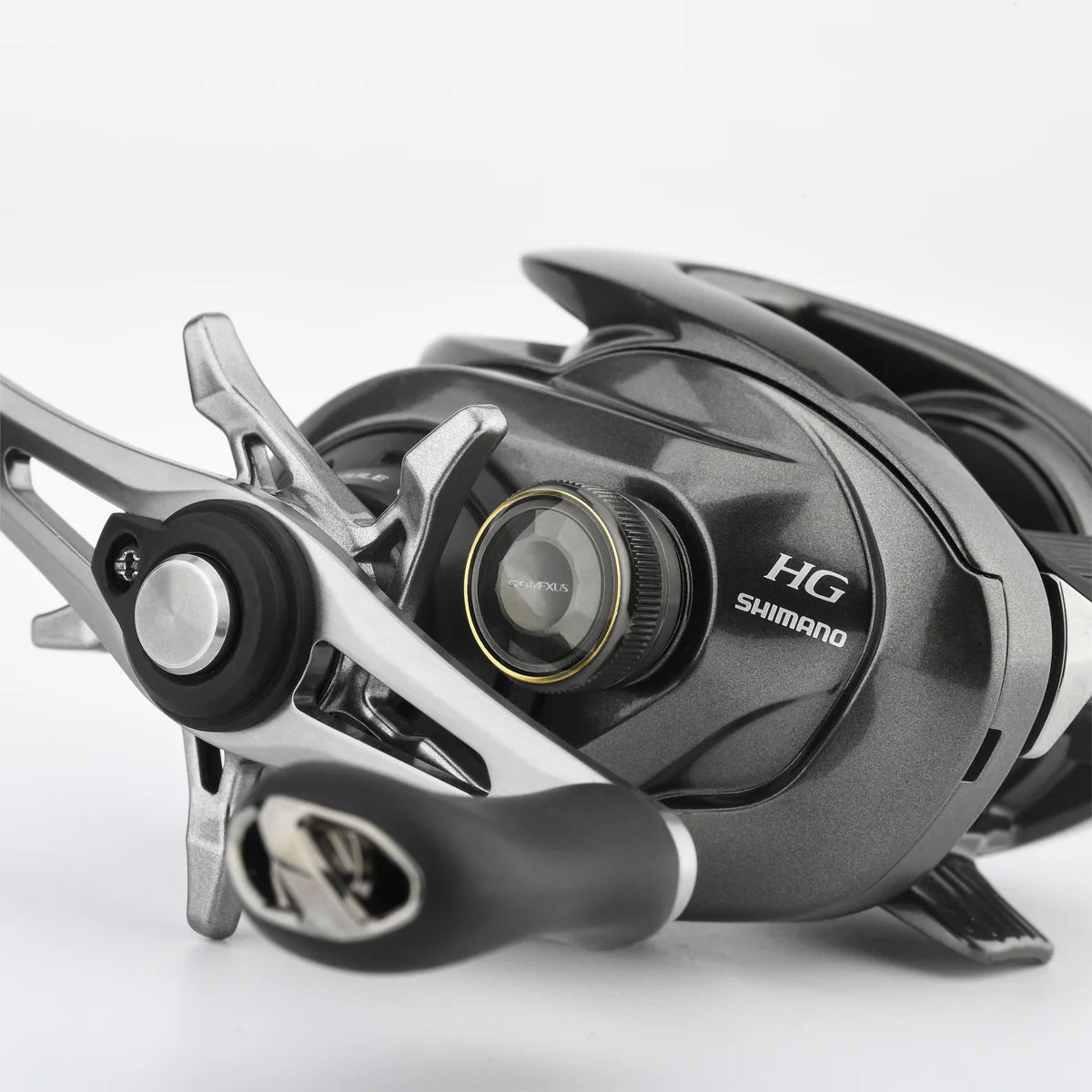 Die Nahaufnahme einer Shimano-Baitcaster-Rolle zeigt die Gomexus Aluminum Spool Tension Knob Cap für 20, 22, 23 Metanium, mit Markendetails auf einem metallischen und schwarzen Gehäuse vor einem schlichten weißen Hintergrund.