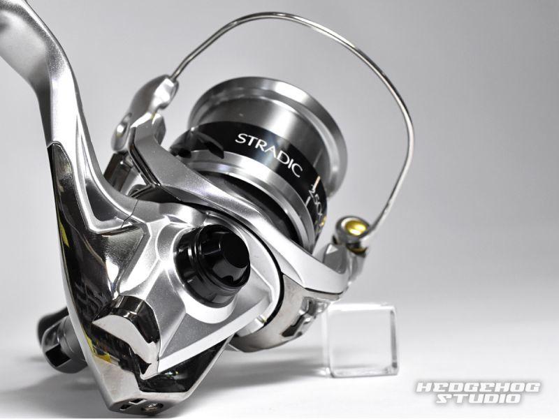 Eine Nahaufnahme einer silbernen Shimano Stradic-Angelrolle zeigt die Hedgehog Studio-Griffschraubkappe mit dem Hedgehog Studio-Logo in der unteren rechten Ecke auf einer weißen Oberfläche.