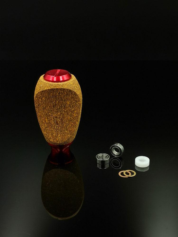 Der RL-TNG Kork Knob von RL-Angelrollentuning besticht durch seine Holzstruktur und die rote Oberseite. Er ist aufrecht auf einer schwarzen, reflektierenden Oberfläche abgebildet und mit zwei Lagern, einem weißen Abstandshalter und zwei goldenen Unterlegscheiben ausgestattet – ideal für Ihr Angelrollen-Setup.
