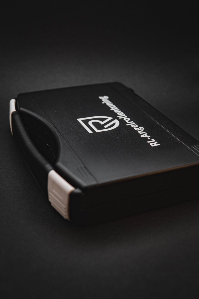 Das RL-TNG Wartungskit Werkzeugkoffer für Baitcaster-Angelrollen von RL-Angelrollentuning ist ein schwarzer Kunststoffkoffer mit weißen Verschlüssen und Logotext auf dem Deckel, perfekt für die Wartung Ihres Baitcasters oder jeder anderen Angelrolle.