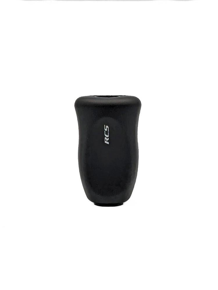 Ein schwarzer, zylindrischer SLP Works RCS i-Shape Korkknopf mit leicht gebogener Form und weißen, vertikal gedruckten RCS-Buchstaben vorne-perfekt für Daiwa Angeln Casting und Spinning Angelrollen, präsentiert auf weißem Hintergrund.