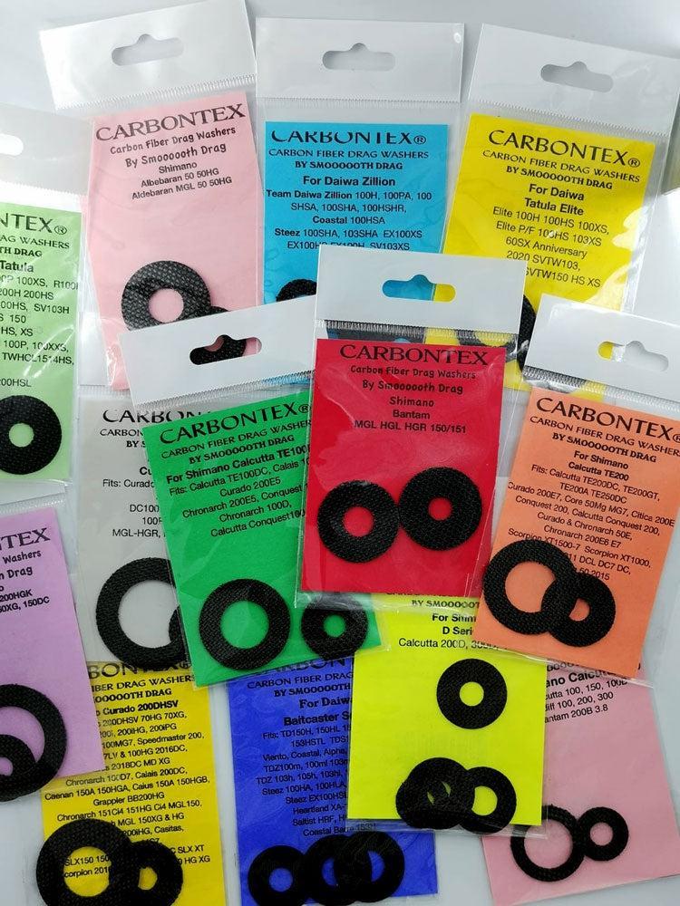 Mehrere Packungen Carbontex-Kohlefaser-Bremsscheiben für Angelrollen sind überlappend auf einer ebenen Fläche angeordnet. Jede Packung enthält Unterlegscheiben in verschiedenen Größen und Farben.