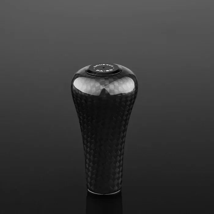Ein schwarzer, strukturierter Gomexus FA30 Carbon-Knopf mit glänzender Oberfläche thront vor dunklem Hintergrund. Oben ziert ein rundes „GENUINE VARIS“-Emblem, das an den Stil dieses Schaltknaufs für Angelrollen erinnert.