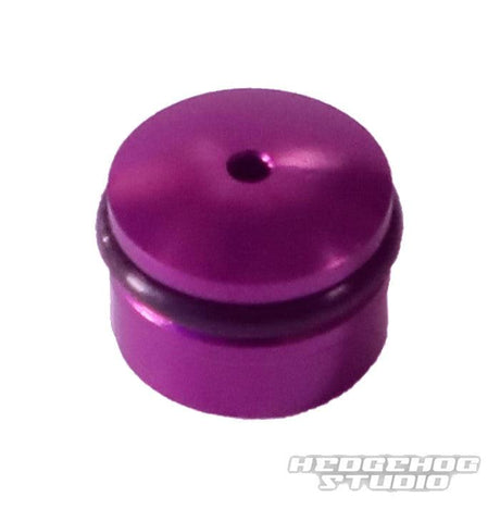 Eine kleine, zylindrische, metallisch-lila Hedgehog Studio-Knopfkappe für Daiwa Finesse-Knöpfe mit einem zentralen oberen Loch und einem schwarzen O-Ring, abgebildet auf einem weißen Hintergrund mit einem schwachen HEDGEHOG STUDIO-Wasserzeichen.
