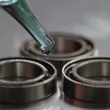 Eine Nahaufnahme einer Pipette, die Glitch Oil High Spec Bearing von Glitch Oil Japan auf Kugellager abgibt, die auf einer metallischen Oberfläche angeordnet sind.