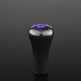 Der Gomexus FA30 Carbon Knob von Gomexus ist ein schwarzer Toray-Carbonfaser-Schaltknauf mit glänzender Oberfläche und einer violetten runden Oberseite mit weißem Text auf einem schwarzen Hintergrund.