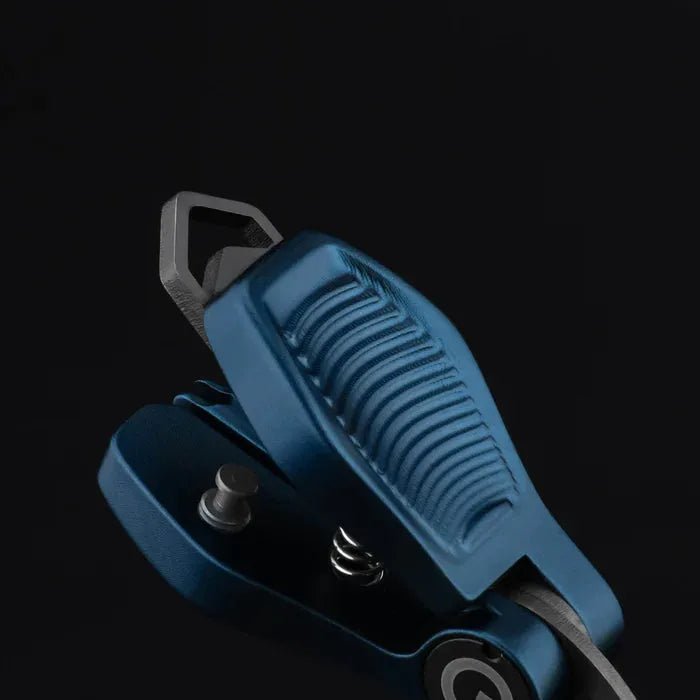 Eine Nahaufnahme des blauen Gomexus SharkBite Schnurknipser Combo mit strukturiertem Griff, sichtbarem Federmechanismus und schwarzer Schlaufenbefestigung von Gomexus vor einem schwarzen Hintergrund.