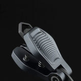 Eine Nahaufnahme des Gomexus SharkBite Schnurknipser Combo, ein graues, strukturiertes Metall-Klappwerkzeug mit geriffeltem Griff, Scharnier und Federmechanismus von Gomexus, vor einem schlichten schwarzen Hintergrund.