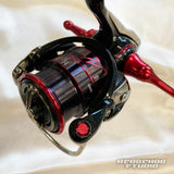 Eine Nahaufnahme einer schwarz-roten Angelrolle „Hedgehog Studio Extra Super Duralumin Schraube für Schnurlaufröllchen“ mit metallischen Akzenten auf einer hellen Oberfläche; die Spule und der Duraluminiumgriff sind sichtbar, mit dem Aufdruck „Hedgehog Studio“ unten rechts.