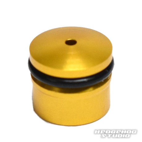 Die Hedgehog Studio Knob Cap | Daiwa Zaion ist ein kleines, zylindrisches Duraluminiumteil in Gold mit einem oberen Loch und einem schwarzen O-Ring. Mit dem Hedgehog Studio Logo versehen, eignet es sich perfekt zum Aufrüsten von Daiwa Zaion Knobs oder zur Verbesserung von Angelrollen.