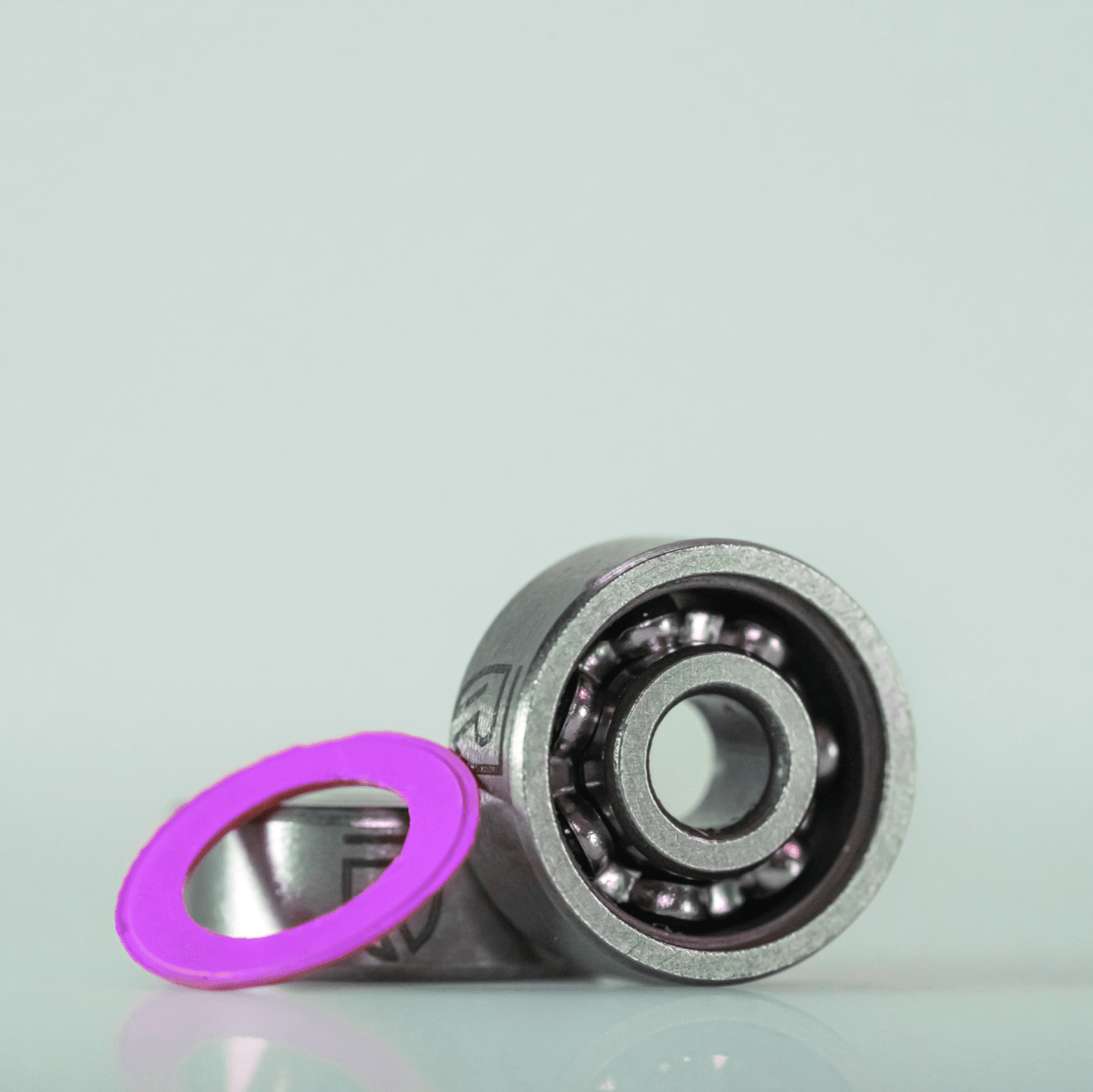 Ein RL-Angelrollentuning RL-TNG Hybrid Keramik Kugellager Set (ABEC 9, Shimano, 5x11x4 & 3x10x4) ruht auf einer hellen Fläche mit einer rosa Dichtung daneben, die das Präzisionstuning für Shimano Baitcaster hervorhebt.