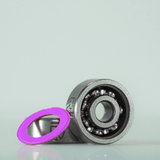 Ein RL-Angelrollentuning RL-TNG Hybrid Keramik Kugellager Set (ABEC 9, Shimano, 5x11x4 & 3x10x4) ruht auf einer hellen Fläche mit einer rosa Dichtung daneben, die das Präzisionstuning für Shimano Baitcaster hervorhebt.