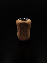 Ein einzelner RL-TNG Kork Knob 20 mm | Griff | Universal Fit von RL-Angelrollentuning mit dunkler Oberseite und Drahtmarkierungen steht aufrecht auf einer glatten schwarzen Oberfläche vor einem schlichten schwarzen Hintergrund.