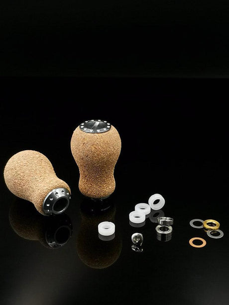 Zwei RL-TNG Kork Knob 20mm Peanut Schaltknäufe von RL-Angelrollentuning mit Metallakzenten werden mit Unterlegscheiben, Muttern und Ringen gezeigt – ideal zum Individualisieren Ihrer Angelrolle oder Ihres Edelstahlkugellagers. Präsentiert auf einer glänzend schwarzen Oberfläche.