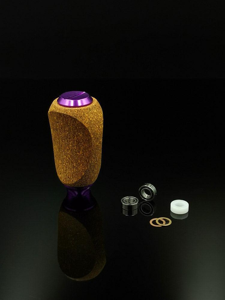 Der RL-TNG Kork Knob von RL-Angelrollentuning, ein mehrfarbiger Universalgriff mit violetten Metallakzenten, steht aufrecht auf einer glänzend schwarzen Oberfläche neben Lagern, Unterlegscheiben und einem weißen Kunststoffring.