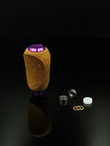 Der RL-TNG Kork Knob von RL-Angelrollentuning, ein mehrfarbiger Universalgriff mit violetten Metallakzenten, steht aufrecht auf einer glänzend schwarzen Oberfläche neben Lagern, Unterlegscheiben und einem weißen Kunststoffring.