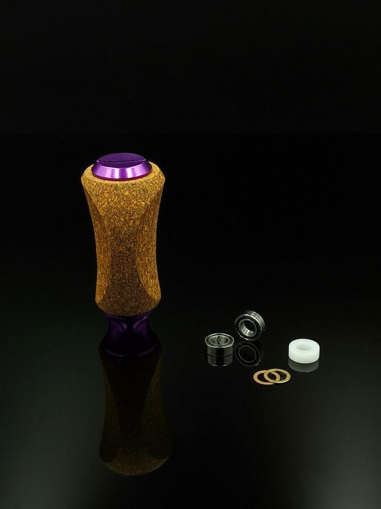 Der RL-Angelrollentuning RL-TNG Kork Knob, ein farbenfroher strukturierter Griff mit universeller Passform, steht aufrecht auf einer reflektierenden Oberfläche neben Metalllagern, Unterlegscheiben und einem weißen Abstandshalter vor schwarzem Hintergrund.