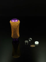 Der RL-Angelrollentuning RL-TNG Kork Knob, ein farbenfroher strukturierter Griff mit universeller Passform, steht aufrecht auf einer reflektierenden Oberfläche neben Metalllagern, Unterlegscheiben und einem weißen Abstandshalter vor schwarzem Hintergrund.