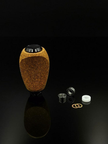 Der RL-TNG Kork Knob von RL-Angelrollentuning, ein strukturierter ovaler Knopf mit universeller Passform in mehreren Farben, steht aufrecht auf einer schwarzen Oberfläche neben Lagern, Unterlegscheiben und einem weißen Kunststoffring.