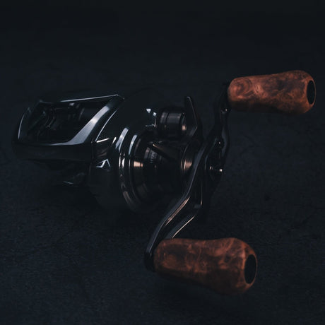 Nahaufnahme einer dunklen, schicken Baitcaster-Rolle mit den legendären SLP Works i Shape Wood Knob Limited Edition Griffen – edles Holz trifft cooles Metall! Das Ganze auf einem stylisch-texturierten Hintergrund, Licht bringt die feinen Details der Holzgriffe und die sexy Kurven Ihrer Tuning-Rolle perfekt zur Geltung. Perfekt für alle, die aus ihrer Angelrolle das Maximum rausholen wollen!.