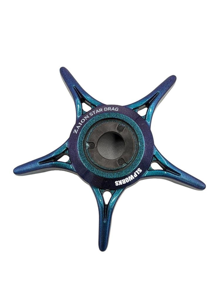 Ein blauer und blaugrüner fünfspeichiger sternförmiger SLP Works Zaion Star Drag aus Metall für Daiwa-Rollen, beschriftet mit "ZL ALON STAR DRAG" und "SUPORMS", ist von oben vor einem weißen Hintergrund zu sehen.