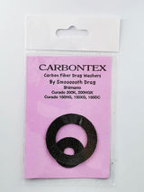 Ein Smoothdrag Bremsscheiben Carbontex-Pack für Shimano Baitcasterrollen enthält zwei schwarze runde Scheiben, die auf einem rosa Hintergrund in einer durchsichtigen Kunststoffverpackung abgebildet sind, und verspricht eine verbesserte Bremskraft für Ihre Angelrolle.
