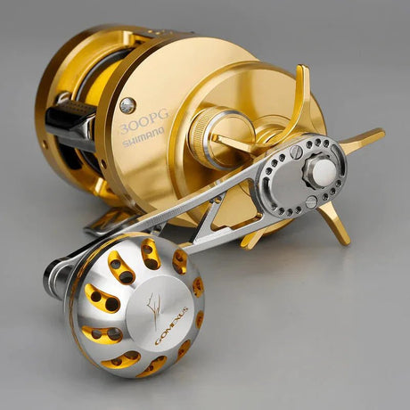Eine goldene Shimano Conquest 300PG-Rolle gepaart mit einem 85-mm-Gomexus-Aluminiumgriff und einem 38-mm-Power-Knopf (7 x 4 mm) in Silber und Gold, aus einem Winkel gezeigt, der die Spule, die Bremseinstellung und die Markendetails zeigt.