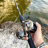 Eine Person steht am Wasserrand und hält eine Angelrute mit einem Gomexus Carbon Handle 75 mm mit 38 mm Power Knob (7x4mm), während die Schnur über das Wasser ragt.