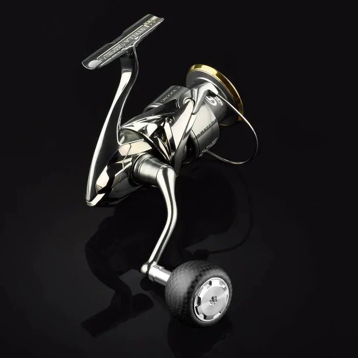 Ein Gomexus Carbon Power Knob 38 mm mit glänzendem Chrom-Finish ist an einer metallischen Angelrolle befestigt, ruht auf einer glänzend schwarzen Oberfläche und reflektiert Licht.